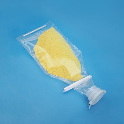 A clear single-use fluid bag filled with yellow powder, shown on a blue background, with a transparent cap and white plastic connector.