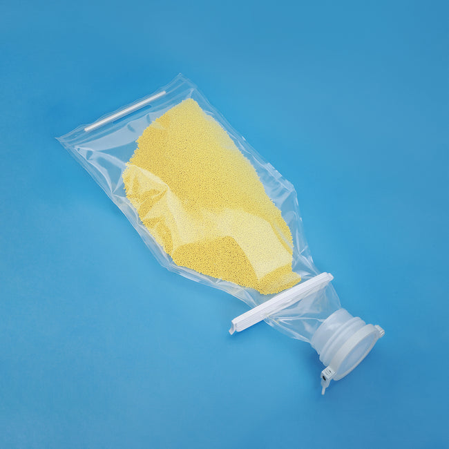 A clear single-use fluid bag filled with yellow powder, shown on a blue background, with a transparent cap and white plastic connector.