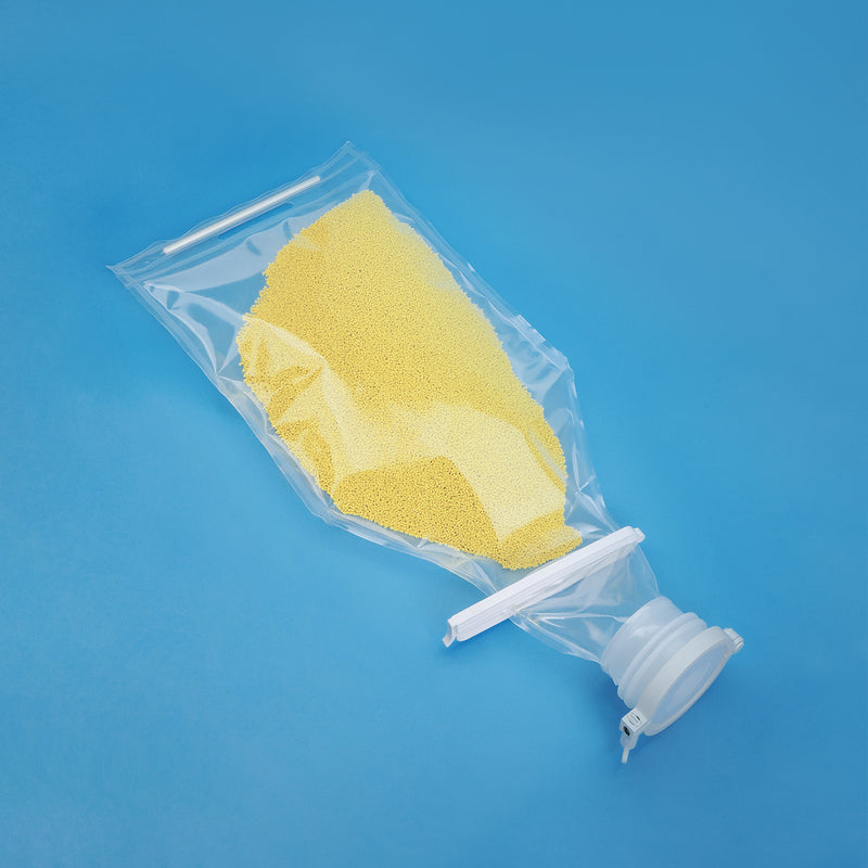 A clear single-use fluid bag filled with yellow powder, shown on a blue background, with a transparent cap and white plastic connector.